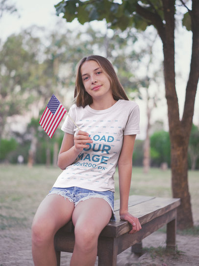 Teen Girl Waving a Little American Flag Wearing a T-Shirt Mockup at the Park