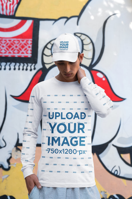 Bella Canvas Long Sleeve Tee and a Dad Hat Mockup of a Serious Man Posing Near a Painted Wall