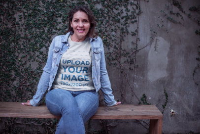 Lady Wearing a T-Shirt Mockup and a Denim Jacket Sitting on a Wooden Bench a20368