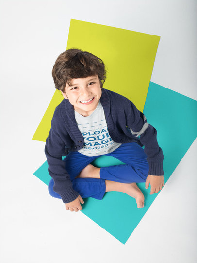 Smiling Kid Wearing a Tshirt Mockup Sitting on Solid Color Pasteboards a19486
