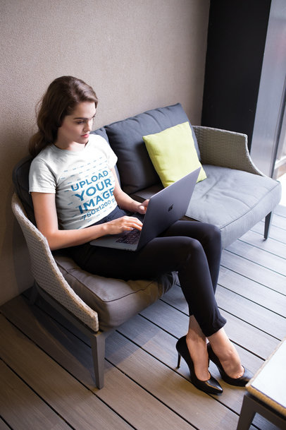 Woman Wearing a Tshirt Mockup Using a Laptop on a Sofa