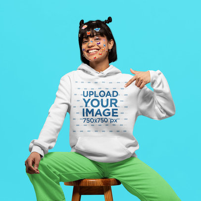 Mockup of a Woman with Face Stickers Pointing at Her Pullover Hoodie