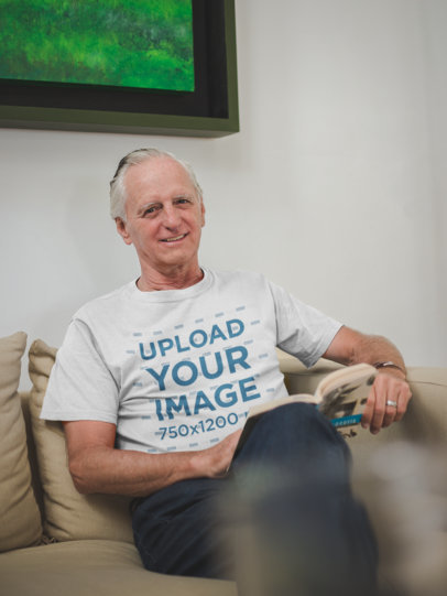 Senior Man Wearing a T-Shirt Mockup Reading a Book Sitting on the Sofa