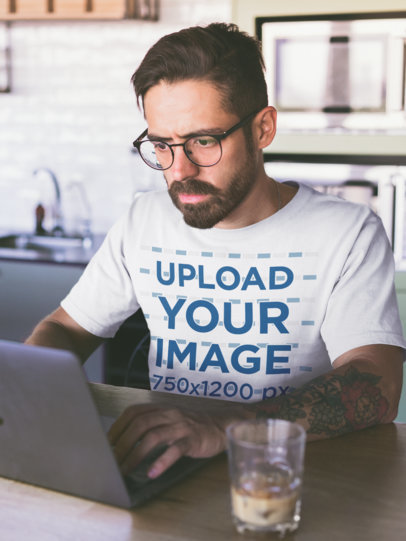 Mockup of a Man Wearing a T-Shirt Working on his Laptop