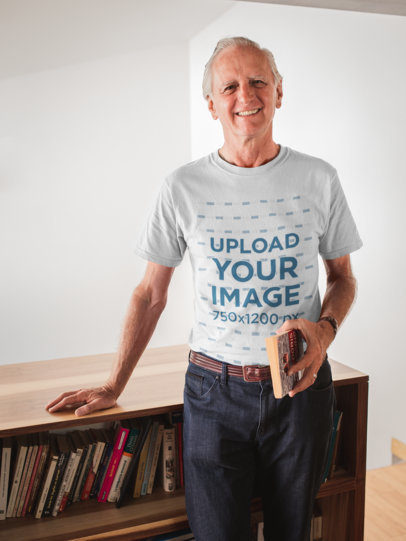 Smiling Man Wearing a Tshirt Mockup Holding a Book in his House