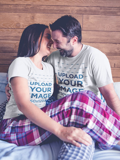 Smiling Couple Wearing Tshirts Mockup while Hugging on Bed