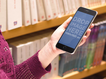 Mockup of a Woman Holding an iPhone 6 Plus at a Library