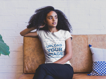 Mockup of a Young Woman with Curly Hair Wearing a T-shirt and nSitting on a Sofa 