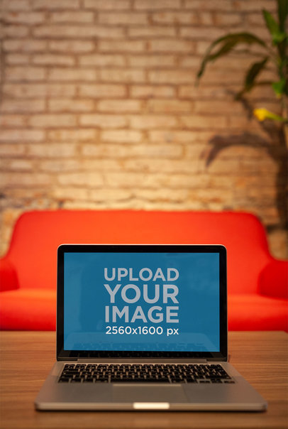 MacBook Mockup Standing on a Wooden Table Against a Red Sofa