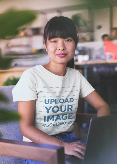 Asian Woman Wearing a Tshirt Mockup Working on a Laptop