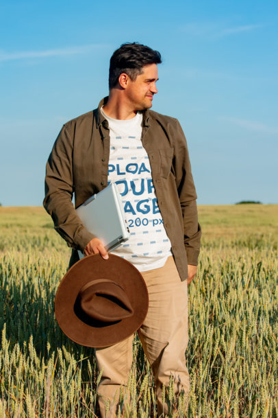 T-Shirt Mockup Featuring a Man Holding a Laptop on a Wheat Field