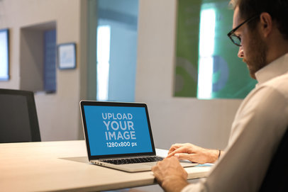 Mockup of a Man Using a MacBook on a Wooden Desk