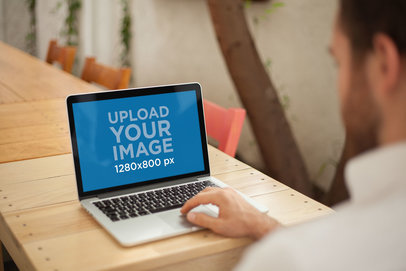 Over-the-Shoulder Mockup of a Man Working with a MacBook on a Wooden Table