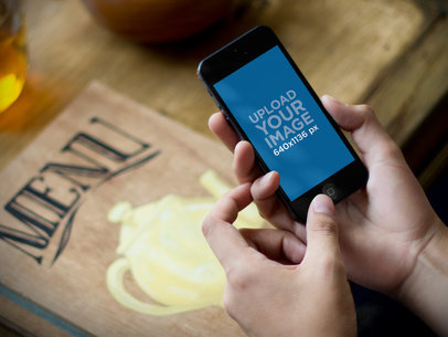 Mockup of a Man Holding an iPhone 5 in a Restaurant m34336