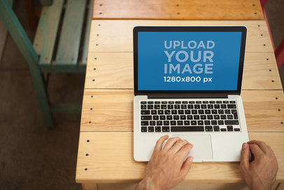 Mockup of a Man Using a MacBook on a Wooden Table