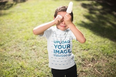 Mockup of a Kid with a Popsicle Wearing a T-Shirt Outdoors
