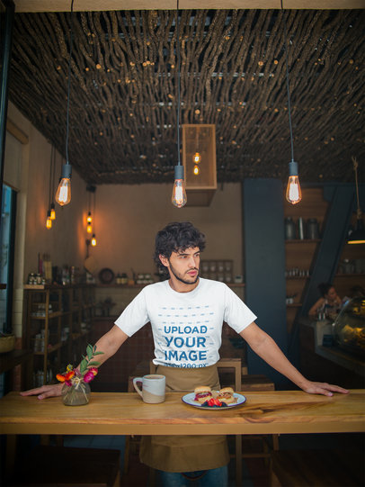 Mockup of a Waiter Wearing a T-Shirt Leaning Against a Wooden Table