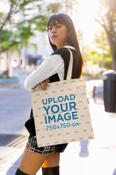 Mockup of a Woman with Long Hair Posing on a Street with a Tote Bag on Her Shoulder