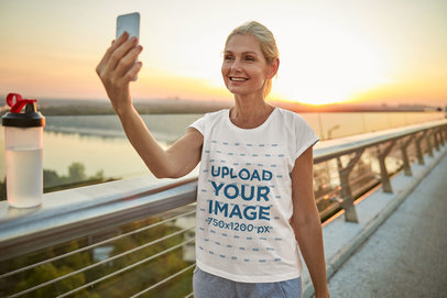 Round-Neck T-Shirt Mockup Featuring a Cheerful Woman Taking a Selfie in a Bridge