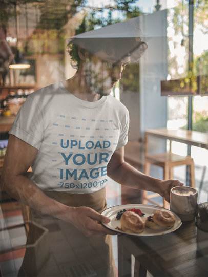 Behind a Window T-Shirt Mockup of a Waiter Wearing a Waist Apron while Serving Breakfast
