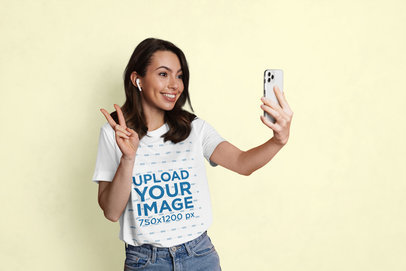 T-Shirt Mockup Featuring a Smiling Woman Taling a Selfie With a Smartphone