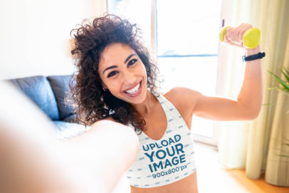 Selfie Mockup of a Woman Wearing a Sports Bra and Holding a Dumbbell at Home