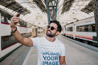 T-Shirt Mockup Featuring a Happy Bearded Man With Sunglasses Taking a Selfie in a Train Station