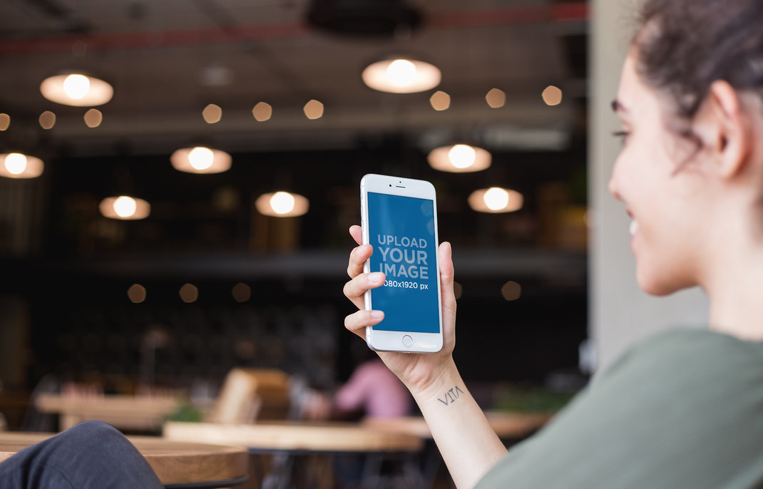 Silver iPhone 8 Mockup Featuring a Happy Woman with a Wrist Tattoo at a Restaurant