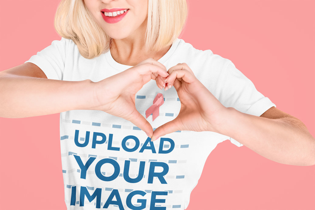 Tee Mockup of a Woman Making a Heart Hand Sign and Wearing a Pink Ribbon for Cancer Awareness