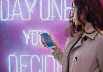 Mockup of a Woman Holding a Rose Gold iPhone 7 Plus by a Neon Sign