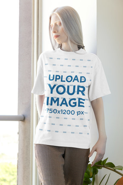 Oversized T-Shirt Mockup Featuring a Serious Woman Posing Near a Window