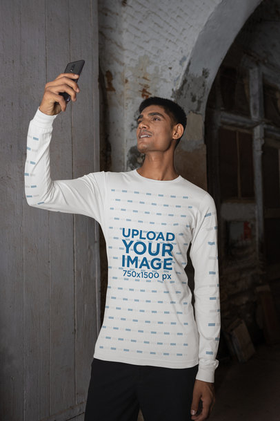 Bella Canvas Long-Sleeve Tee Mockup Featuring a Man Taking a Selfie by an Old Building