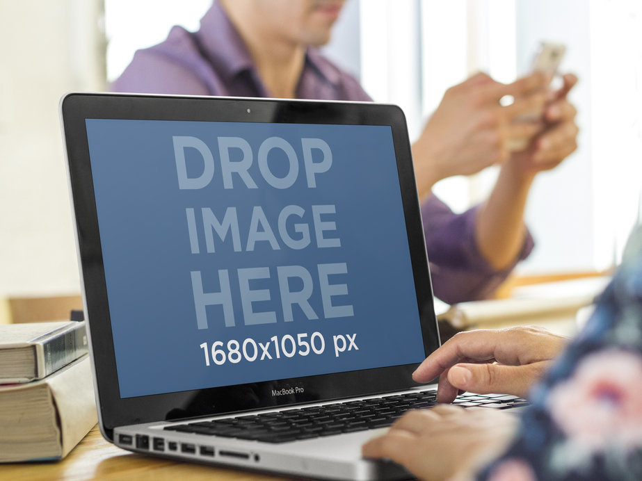 Macbook Pro Mockup Featuring a Woman Working While Coworker is Texting