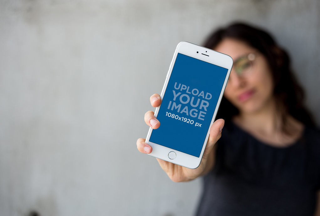 Mockup of a Woman Holding a Silver iPhone 8 Plus Against a Concrete Wall
