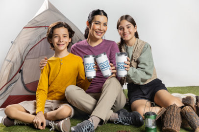 Mockup of a Woman With Two Kids Holding Travel Mugs While Sitting Against a Tent