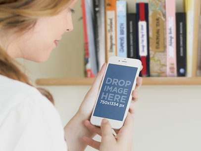 Mockup Featuring a Woman Using a White iPhone 6 by a Bookshelf