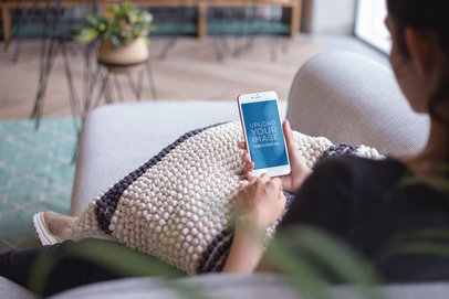 Mockup of a Woman Using a Rose Gold iPhone Sitting on a Sofa