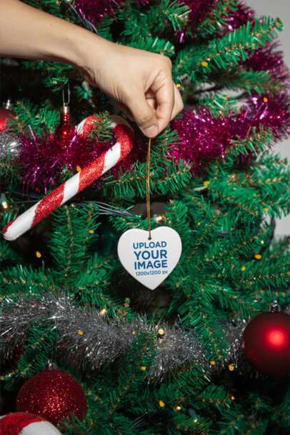 Mockup of a Person Holding a Heart-Shaped Ornament Against a Christmas Tree