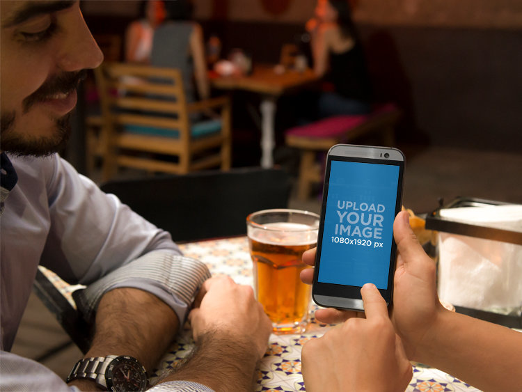 Mockup of a Woman Showing Her Android to a Man at a Restaurant