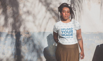 Sublimated T-Shirt Mockup of a Tattooed Woman with Locs Against an Old Wall
