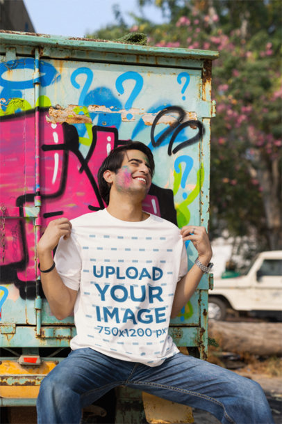 Blinkstore T-Shirt Mockup of a Cheerful Man Sitting Against a Painted Truck in a Holi Celebration