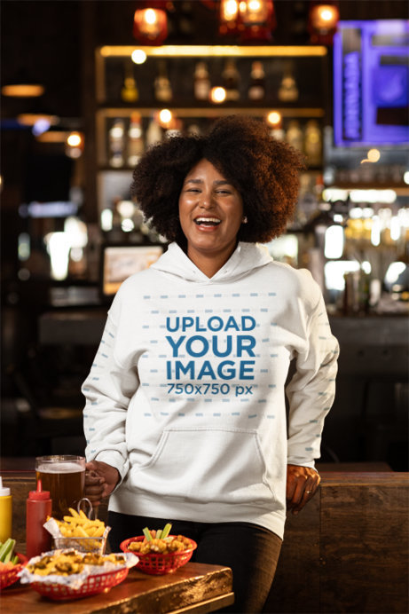 Gildan Pullover Hoodie Mockup of a Happy Woman Having Food and Drinks in a Sports Bar