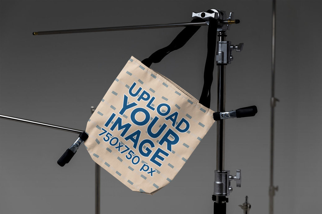 Mockup of a Sublimated Tote Bag Hanging From a Steel Tripod