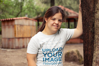 Round Neck Tee Mockup Featuring a Woman Leaning Against a Tree with One Arm