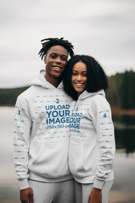 AI-Created Mockup of a Smiling Couple Wearing Matching Hoodies in Front of a Lake