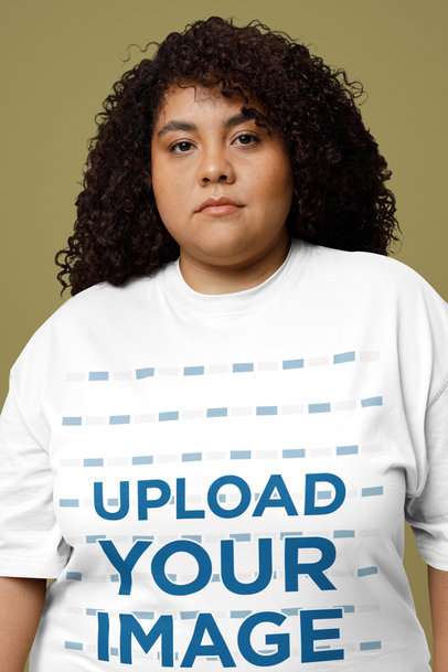 Oversized T-Shirt Mockup Featuring a Curly-Haired Woman Posing With a Serious Look in a Studio