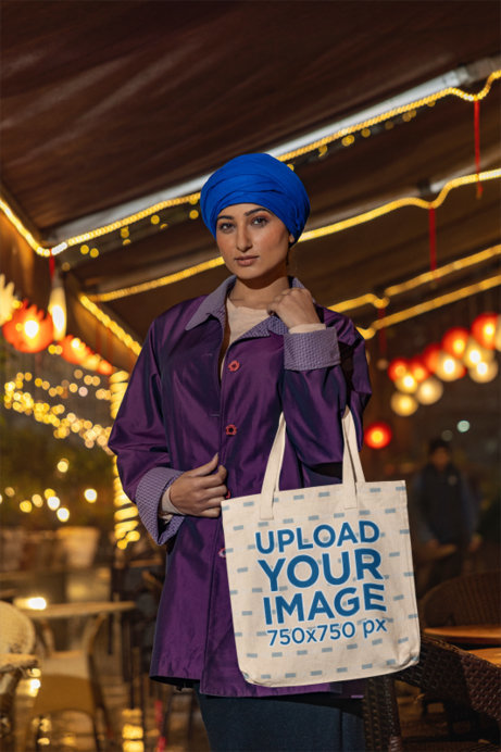 Tote Bag Mockup Featuring a Woman Wearing a Turban and a Posing in the Street