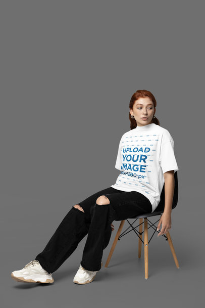 Oversized T-Shirt Mockup Featuring a Woman Sitting on a Black Chair in a Studio