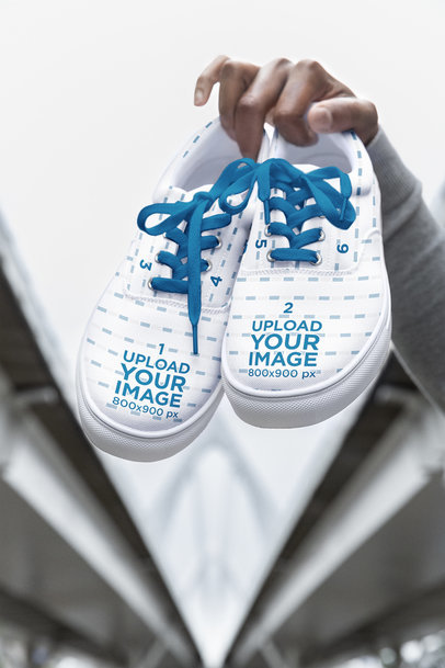 Mockup of a Man's Hand Holding a Pair of Low Sneakers m38267