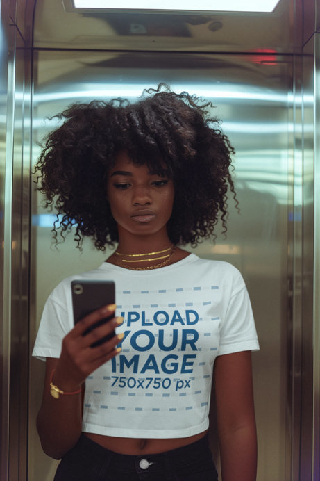 T-Shirt Mockup of a Woman with an Afro Hairstyle Taking a Selfie in an Elevator